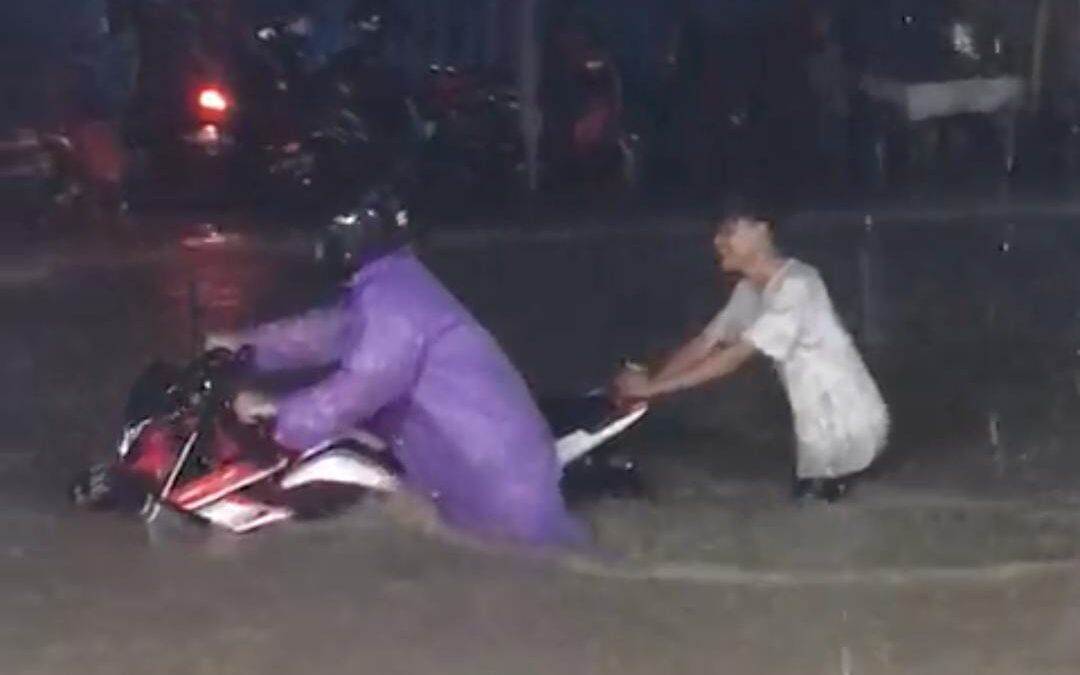 Tangkapan layar dari video yang beredar, memperlihatkan pengendara motor yang dibantu warga sekitar saat mendorong motornya akibat banjir (Foto: Istimewa)
